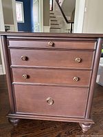 Front view of the custom solid wood bedside table showing three drawers with brass knobs and polished wood finish.