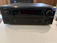 Front view of Denon AVR 2105 7.1 channel AV receiver showing volume and tuning knobs, input display, and control buttons.