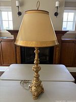 Full view of the lamp standing on white table in front of dark fireplace and wood cabinetry, showing entire lamp and shade.