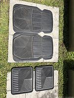 Top view of two larger front black rubber car mats placed side by side on outdoor stone floor.