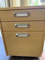 Front view of the wooden filing cabinet showing three drawers with metal handles and label holders.