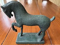 Full side view of bronze horse sculpture on wooden table showing base and posture.