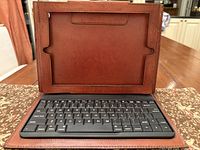 Natural brown leather case with integrated keyboard open, front view showing slot for iPad and keyboard layout