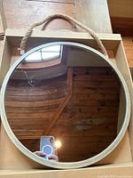 Top view of round wall mirror in box showing overall size and sage green metal edge with attached rustic rope hanger.