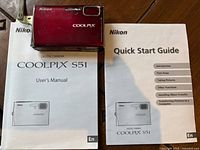 Red Nikon Coolpix S51 digital camera on top of user manuals showing front, model and brand name.