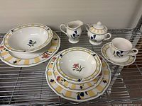 Full set of Noritake Summer Estate dishes arranged on metal shelving including plates, bowls, cups, cream jug, and sugar bowl.