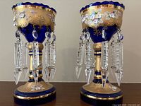 Front view of both lustres showing overall shape, scalloped rims, gilt decoration and hanging prisms