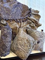Set of reversible chenille throw and three pillows arranged on bed showcasing paisley patterns and tassels