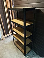 Front angle view showing full shelving unit with five wood shelves and black metal frame against a wall.