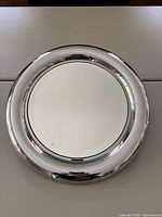 Front-facing photo showing the round mirror with a thick shiny stainless steel frame and the mirror center reflecting the room.