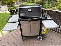 Front-angle view of Weber Genesis Silver grill on deck showing side trays and cabinet doors