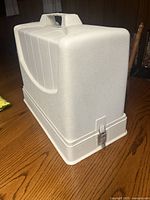 White hard plastic carrying case for sewing machine, closed and latched with handle on top