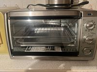 Black & Decker convection countertop oven with visible glass door, wire racks, and three control dials.