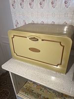 Closed yellow cedar bread box showing front with wooden handle and decorative border.