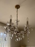 Full view of the chandelier hanging from the ceiling; shows bronze colored chain and ceiling mount, five glass arms, and candle-flame shaped bulbs.