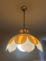 Floral hanging ceiling light with petal-shaped panels in white and yellow colors illuminated and hanging from ceiling chain.