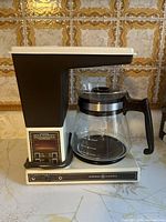 Front view of General Electric coffee maker with glass carafe showing programmable timer panel and carafe on heating base.