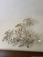Full view of gold metal botanical wall sculpture mounted on wall above furniture.