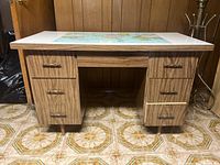 Front view of a mid-century laminate desk with wood grain drawer fronts and a white top featuring a world map graphic. Six drawers with metal handles.