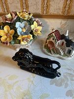 Multicolor flower basket, white cottage with red roof, and black lion figurines shown