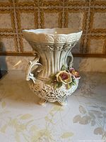 Front view of the white ceramic vase showing detailed floral decorations and ornate handle on one side.