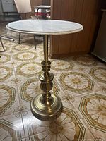 Full view of round side table with white marble top and brass base on a tiled floor.