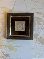 Front view of framed art tile featuring woman's profile in relief, wood frame with gold accents.
