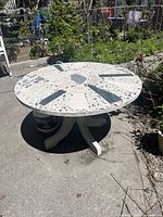 Full view of round terrazzo table outdoors showing the table top and its base on concrete surface with garden background.