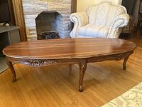 Photo of full view of traditional brown wood coffee table showing carved details on apron and legs.