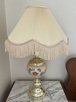 Front view of one table lamp showing pleated cream fabric shade with fringe and floral ceramic base.