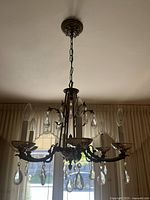 Full view of vintage brass chandelier suspended from ceiling with 5 candle-style lights and hanging crystal accents.