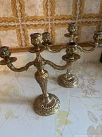 Pair of vintage brass three-arm candelabras photographed on a countertop with tiled backsplash.