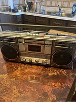 Front view of the silver JVC cassette player showing buttons, cassette slot, and speaker grills