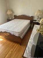 Full view of queen size wooden bed with mattress and two side tables with marble tops on each side, positioned against a plain wall.
