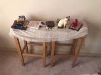 Two wooden bar stools side-by-side, lace cloth on top, assorted items including cat figurine, album, incense visible