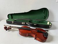View of violin, violin case with green interior lining, and wooden bow lying outside the case