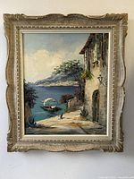 Full front view of the framed oil painting depicting the coastal scene, showing details and condition including craquelure and small hole.
