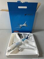 Top view of unassembled Boeing 787 model airplane in styrofoam packaging with blue branded box in background.