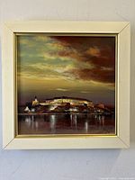 Front of framed broody oil painting on canvas with dramatic sky and building on shoreline, artist signed bottom right.