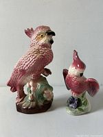 Both intact figurines, pink hued exotic birds, one larger at 9x5.5 inches, smaller at 6.5x4.25 inches