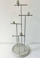 Silver metal jewelry display stand with multiple small owl figures perched on horizontal bars at different heights. Standing on a round weighted base.