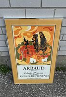 Framed French Arbaud 'Lumieres' art poster with a warm color palette and exhibition text in French, standing against a wall outdoors
