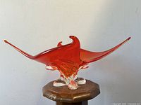 Front view of red-hued asymmetrical art glass bowl with pointed ends on a wooden pedestal.