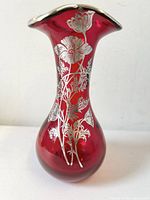 Front view of ruby red art glass vase with silver overlay poppy floral design and trefoil top.