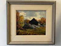 Framed full view of oil painting on board showing rustic cabin, rocks, and autumn trees under cloudy sky.
