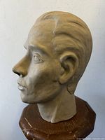 Side profile of the lifesize sculpted man's head statue showing detailed facial features and slate grey surface color with crack marks.