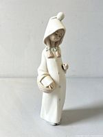 Front view of the porcelain girl figurine wearing a hooded coat with pom-pom, holding a basket in the left hand.