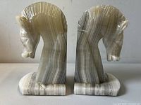 Pair of carved onyx horse head bookends resembling knight chess pieces, showing front and side profiles with polished banded onyx surface and detailed carving.