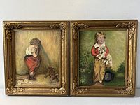 Pair of framed oil paintings depicting children with dogs in gilt wood frames hanging on white wall.