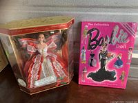 10th Anniversary Holiday Barbie Doll in original box standing beside the 40th Anniversary Collectible Guide Book with pink cover featuring Barbie dolls.